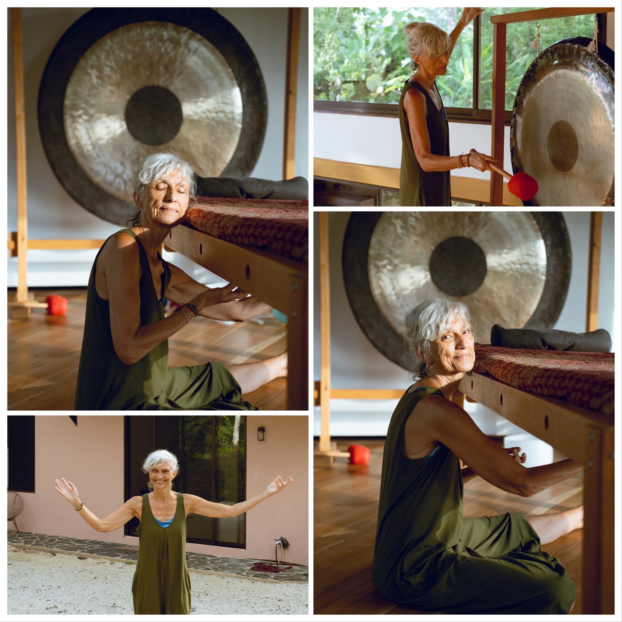 A woman with gray hair in a green dress plays a large gong and sits smiling on the floor in a bright room, with trees visible outside. In one photo, she stands outside with arms open, appearing joyful.