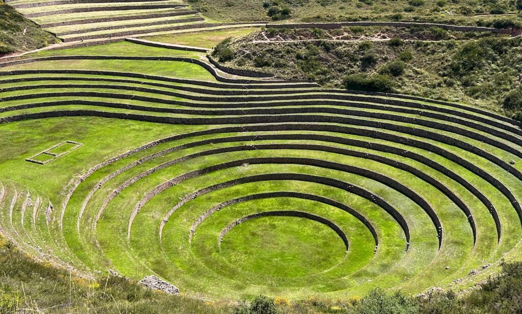 Aerial view of Moray, an ancient Incan archaeological site in Peru, featuring concentric circular terraces carved into green hillsides used for agricultural experiments.